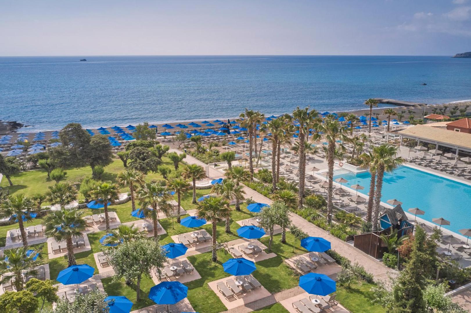 Esperides Beach Resort zaļā dārza zona ar sauļošanās krēsliem, ziliem saulessargiem un skatu uz Vidusjūru