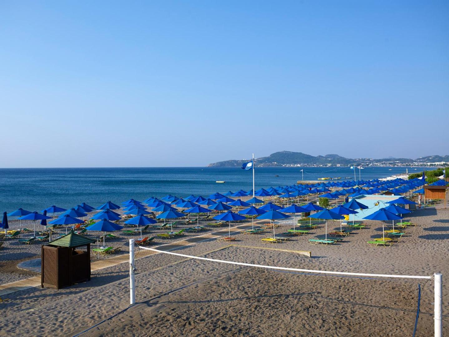 Esperides Beach plašā smilšu un oļu pludmale Rodā ar ziliem saulessargiem, pludmales volejbola tīklu un skatu uz jūru