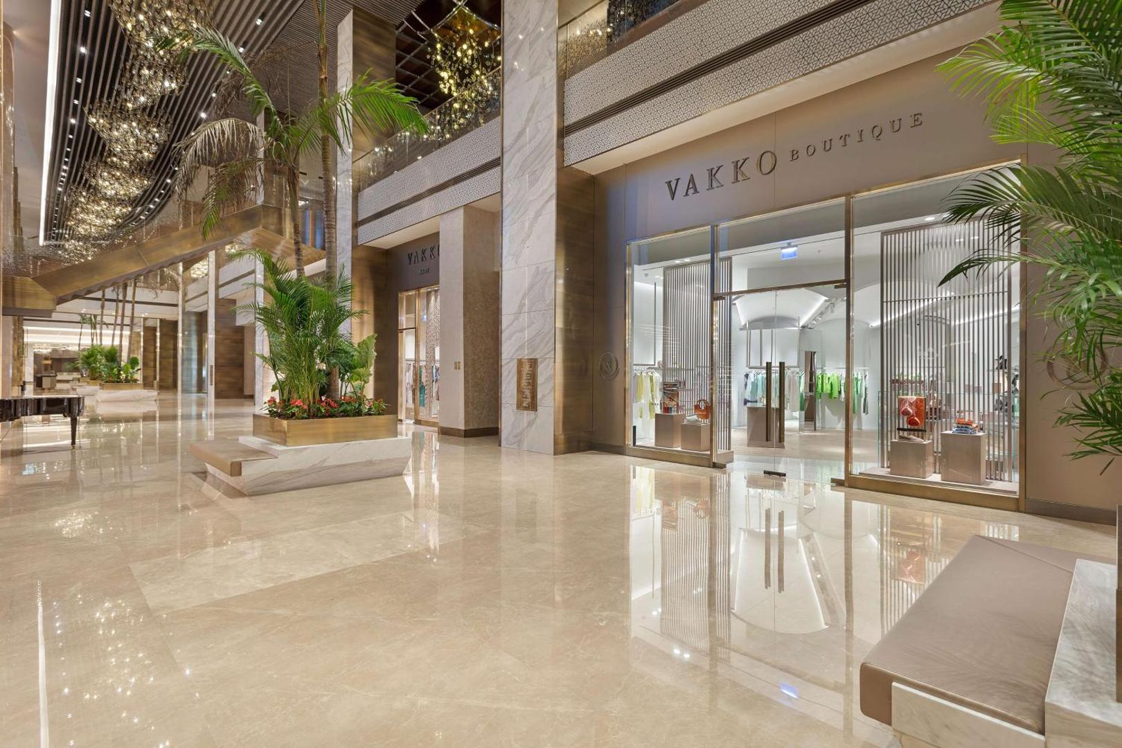 Cullinan Golf & Resort viesnīcas plašais vestibils ar marmora grīdām un luksusa boutique veikalu Belekā, Turcijā — elegants interjers ar palmām.