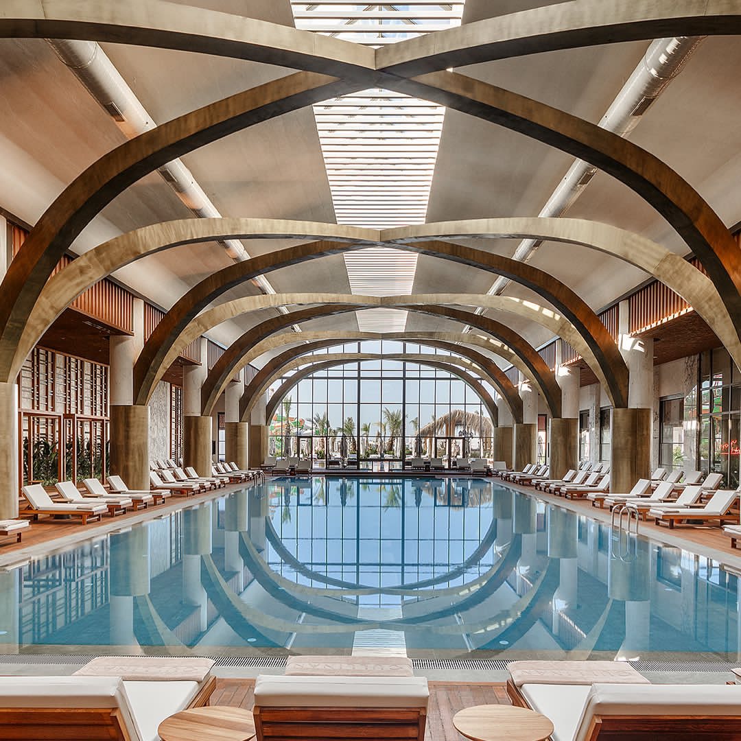 Cullinan Golf & Resort elegantais iekštelpu baseins ar augstām koka arkām, panorāmas logiem un ērtiem guļamkrēsliem spa zonā