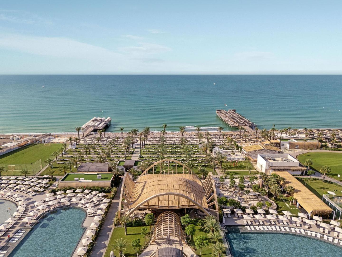 Cullinan Belek Resort panorāmas skats no augšas uz plašo teritoriju, baseiniem, smilšu pludmali un diviem koka tiltiem Vidusjūras krastā.