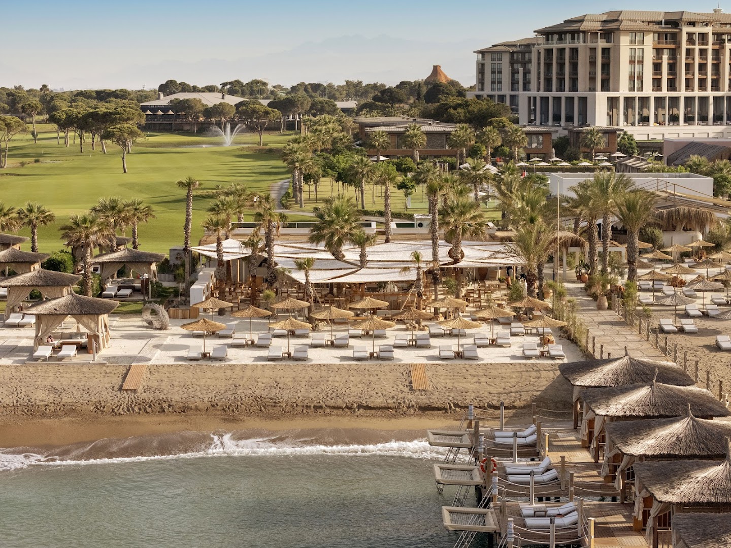 Cullinan Golf & Resort pludmales klubs ar saulessargiem, sauļošanās krēsliem un skatu uz blakus esošajiem golfa laukumiem Belekas piekrastē.