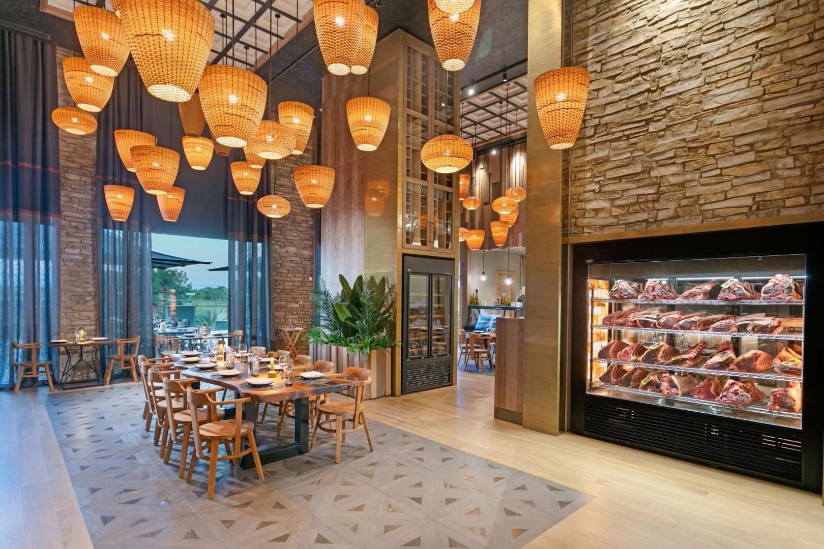 Cullinan Golf & Resort gaļas restorāna interjers ar modernām klūgu lampām, akmens sienām un nogatavinātas gaļas vitrīnu.