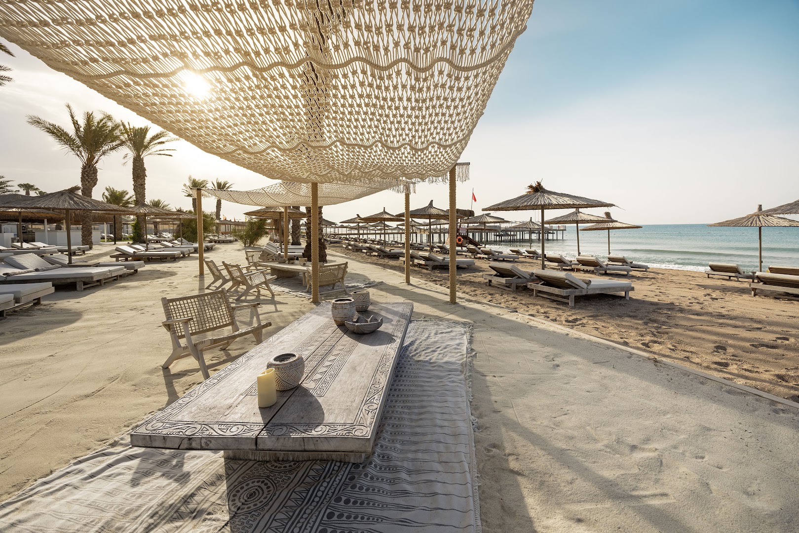 Cullinan Golf & Resort privātā pludmale Belekā ar boho stila saulessargiem, koka galdiem un ērtiem zviļņiem Vidusjūras krastā.