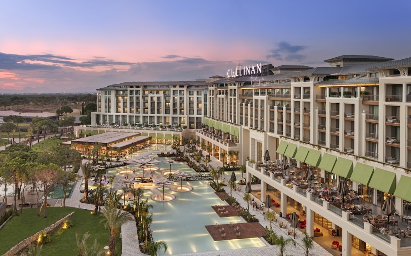Cullinan Golf & Resort modernā arhitektūra un baseinu zona vakara apgaismojumā ar skatu uz apkārtējo dārzu un priežu mežu.