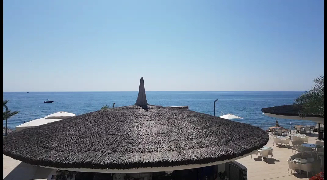 Corendon Playa Kemer viesnīcas āra terase ar bāru un saulessargiem piekrastē — skats uz Vidusjūras zilo horizontu un atpūtas zonu