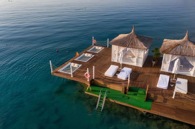 Corendon Playa Kemer laipa ar baltiem bungalo un tīkliem atpūtai virs ūdens — kristāldzidrs jūras ūdens un sauļošanās zona