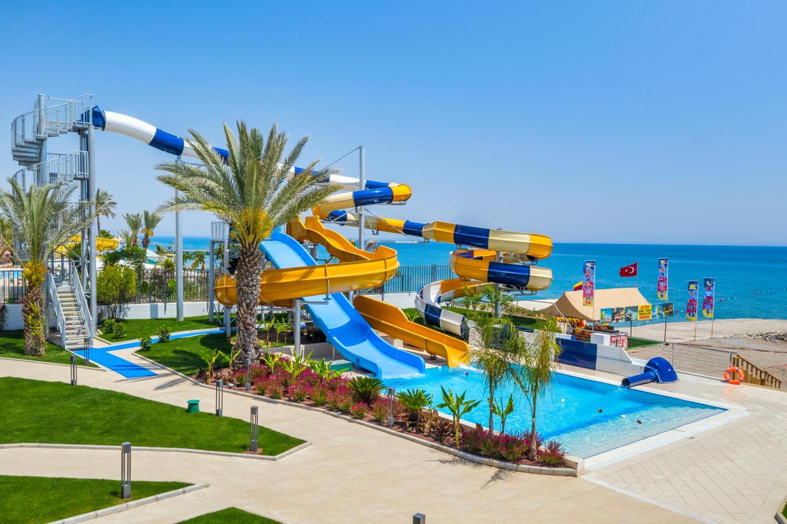 Corendon Playa Kemer ūdens slidkalniņi un bērnu baseins pie jūras krasta Kemeras reģionā — krāsainas atrakcijas un palmas