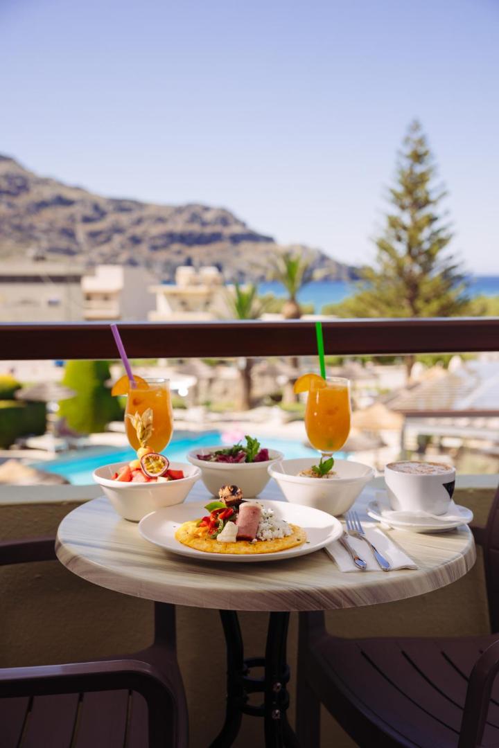 Brokastis uz Alianthos Garden Hotel balkona ar skatu uz jūru un kalniem — svaigi augļi, omlete un kafija saulainā rītā