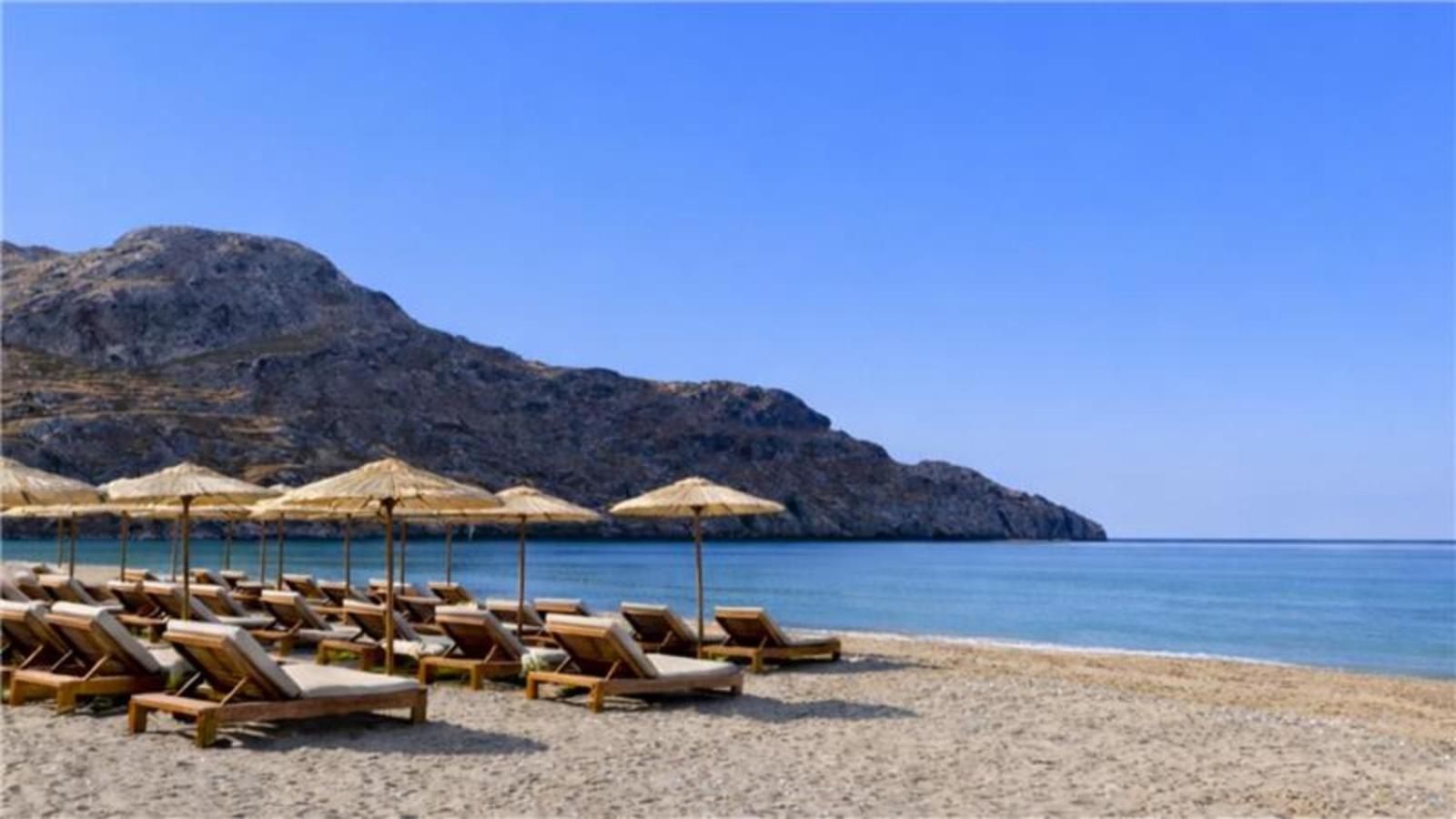 Alianthos Garden Hotel privātā pludmale ar saulessargiem un zviļņiem Plakiasas līcī, Krētā — skats uz kalniem un jūru