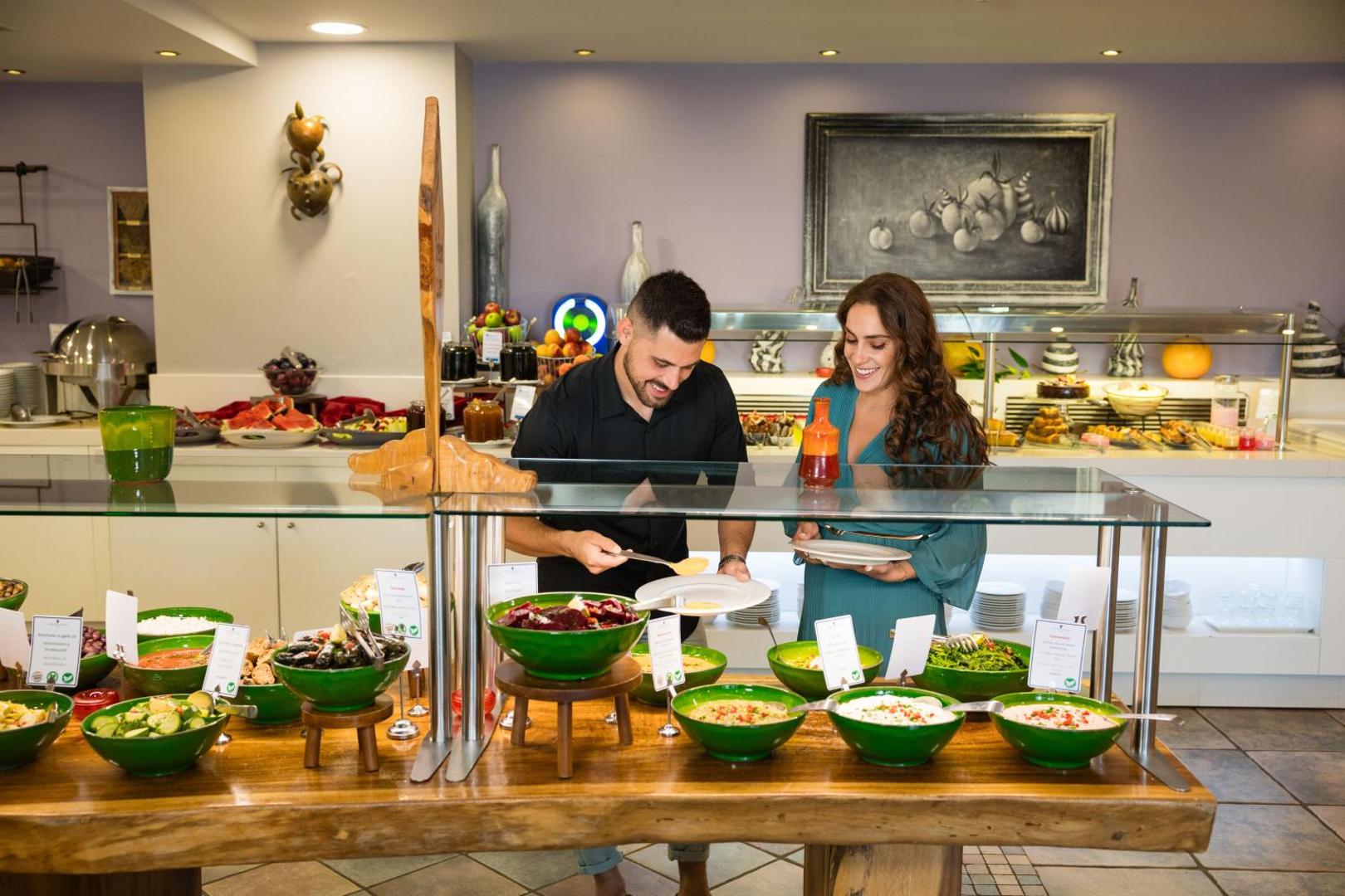 Alianthos Garden Hotel bufetes tipa restorāns ar plašu uzkodu un salātu izvēli — viesi izvēlas ēdienus pie koka galda