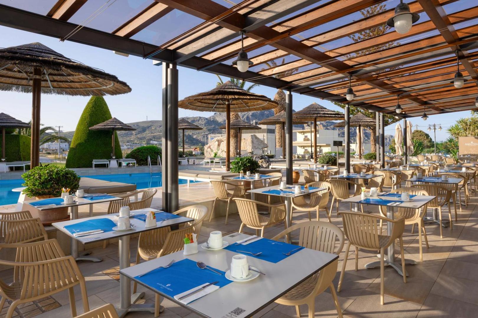 Alianthos Garden Hotel āra restorāna terase ar skatu uz baseinu un kalniem Plakiasā, Krētā — galdiņi zem koka nojumes