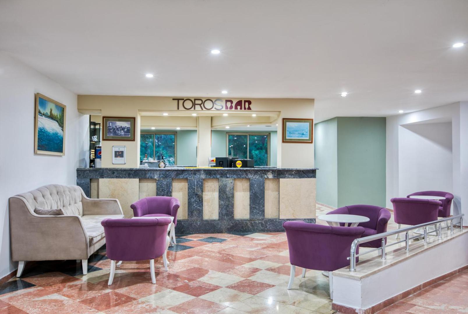 Asteria Collection Side viesnīcas Toros Bar atpūtas zona ar violetiem krēsliem un gaišu dīvānu pie marmora bāra letes