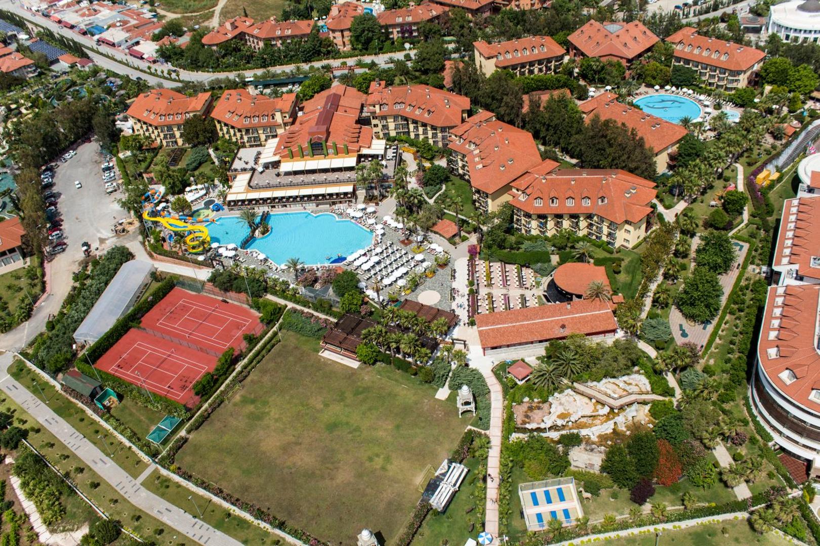 Alba Resort Hotel teritorijas skats no augšas ar lielu āra baseinu, ūdens slidkalniņiem, tenisa kortiem un dārza ieskautiem numuru korpusiem