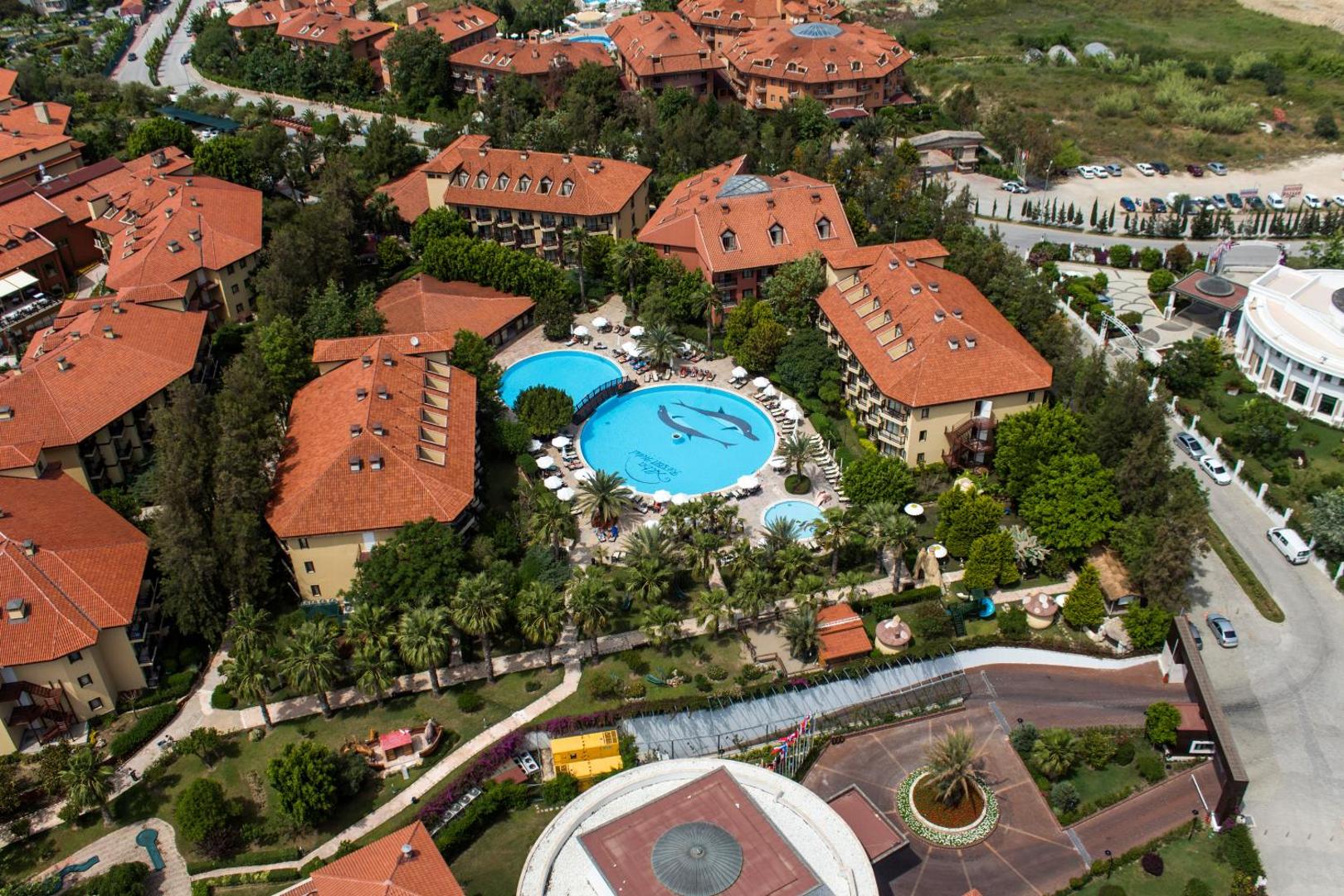 Alba Resort Hotel skats no putna lidojuma uz baseinu ar delfīnu zīmējumu, ēkām ar sarkaniem jumtiem un dārzu.