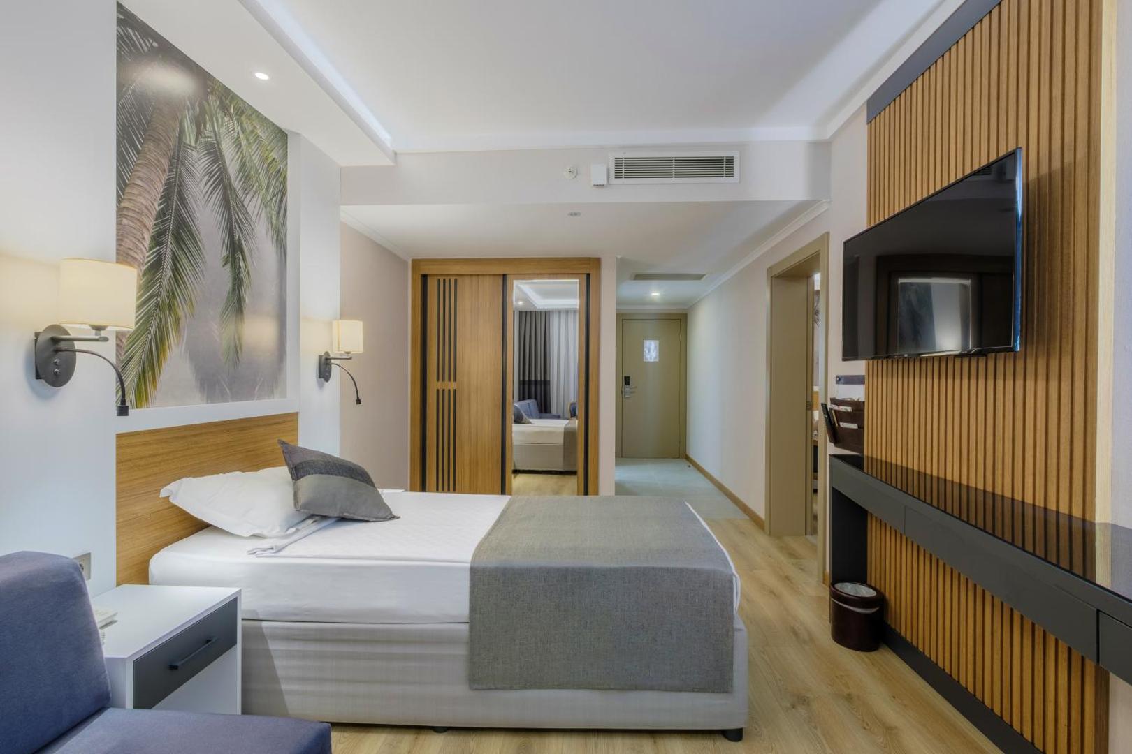 Alba Resort Hotel plašs numurs ar gultu, dīvānu, sienas televizoru un koka apdari Sides kūrortā Turcijā