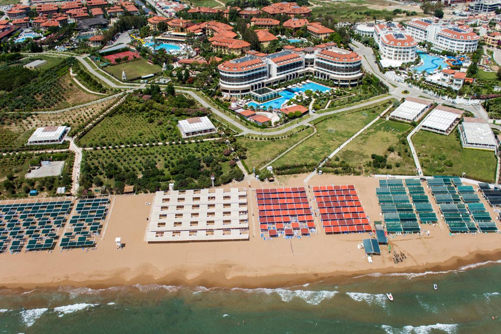 Alba Resort Hotel panorāmas skats no putna lidojuma uz plašo smilšu pludmali, saulessargiem un viesnīcas korpusiem Sides reģionā, Turcijā