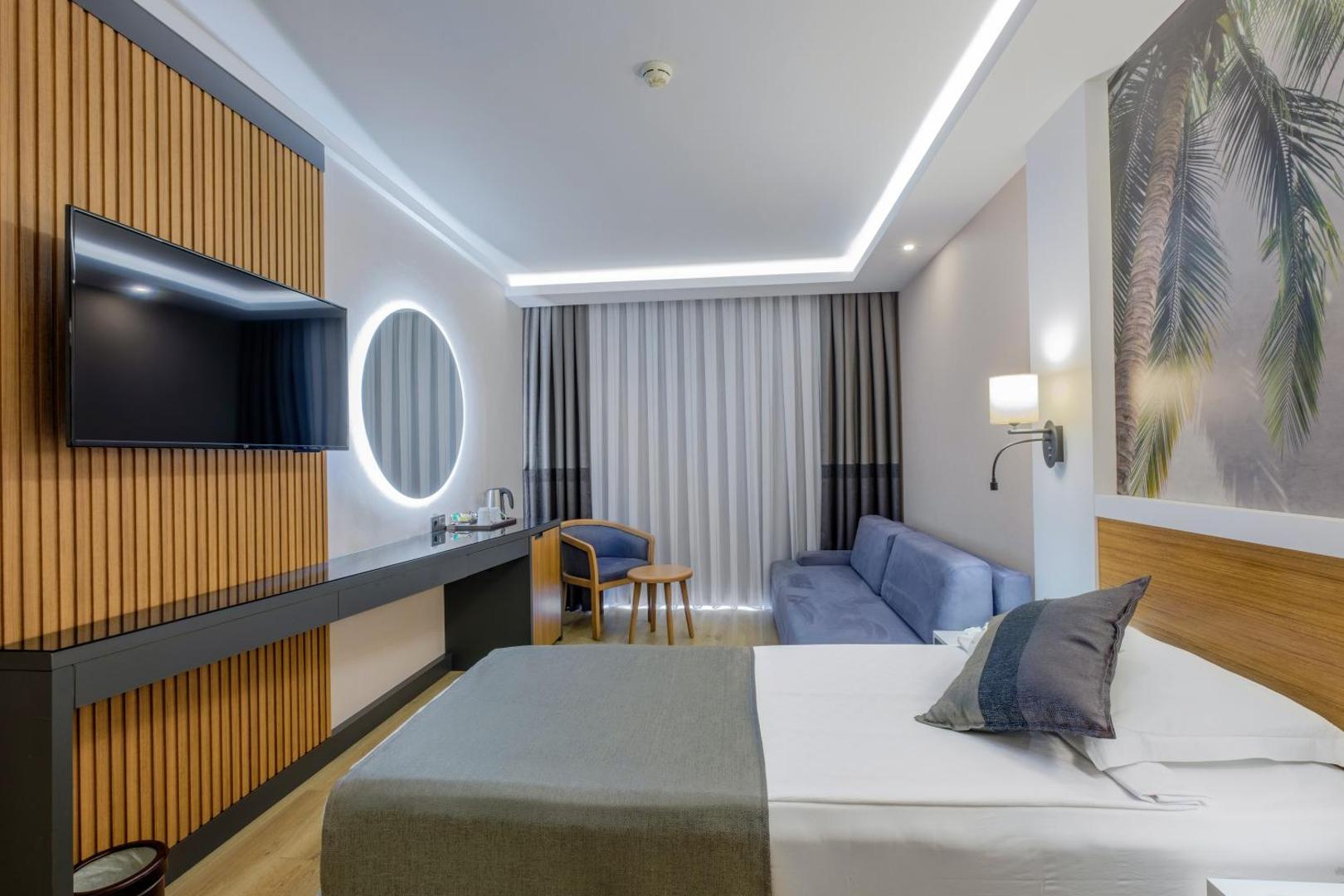 Alba Resort Hotel numura interjers ar zilu dīvānu, izgaismotu spoguli un modernu koka sienas paneli Sides reģionā