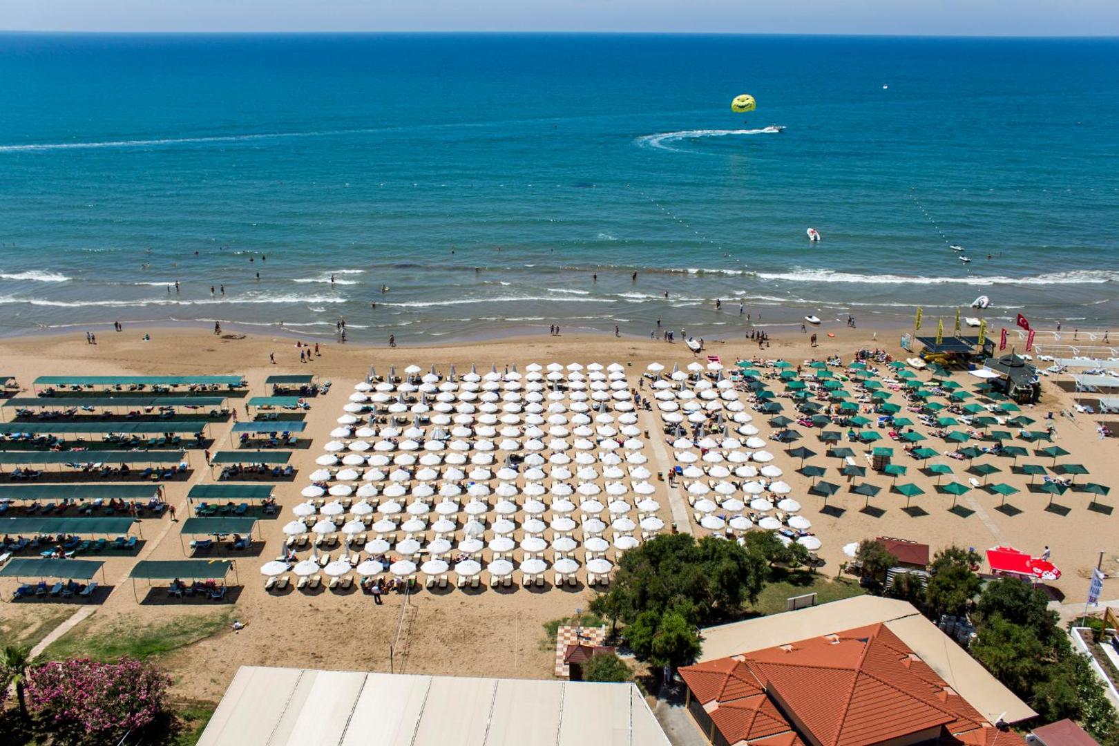 Alba Resort Hotel pludmales zona ar saulessargiem un ūdens sporta aktivitātēm Vidusjūrā — redzams izpletņa lidojums virs ūdens