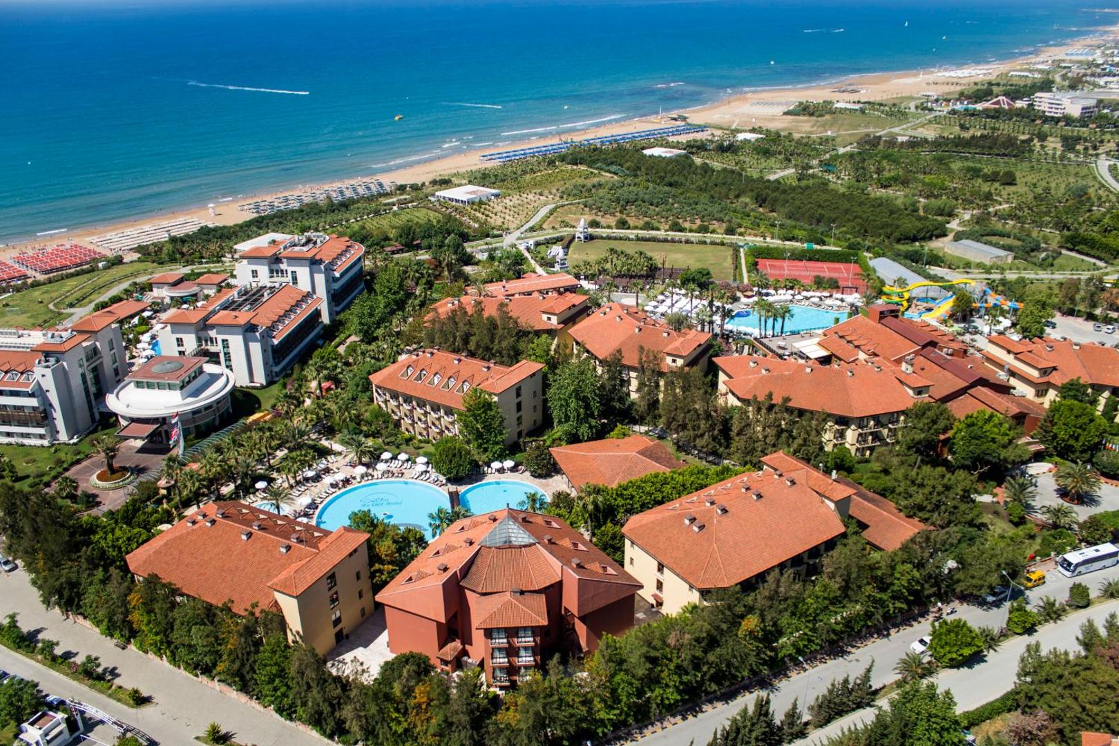 Alba Resort Hotel teritorijas aerofoto ar vairākiem baseiniem, zaļo zonu un tiešu piekļuvi plašajai Vidusjūras piekrastei