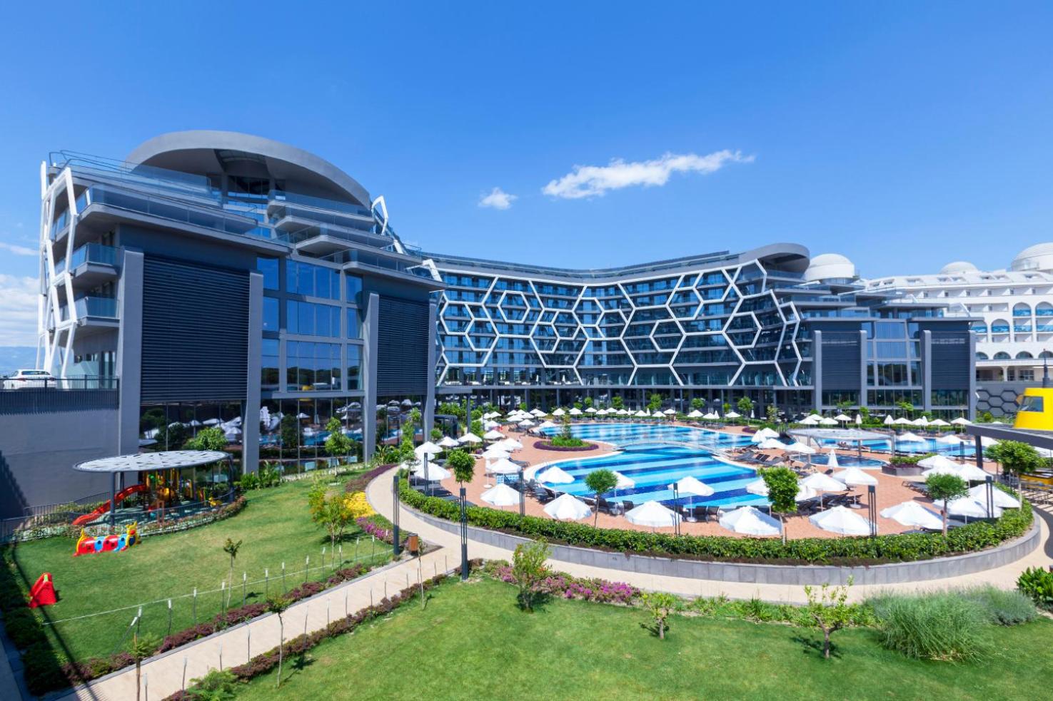 Bosphorus Sorgun Hotel ēkas skats no dārza puses dienā — redzams zaļš zāliens, bērnu rotaļu laukums un galvenais baseins