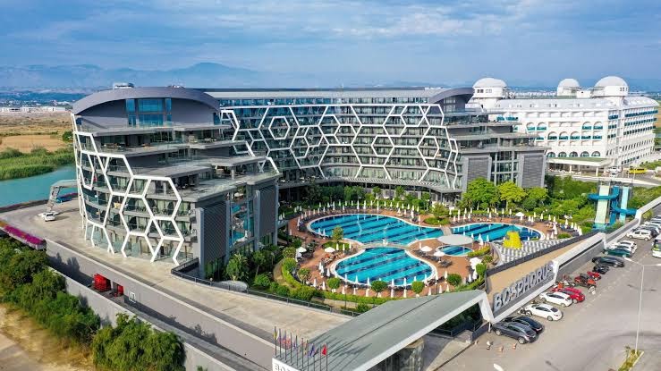 Bosphorus Sorgun Hotel pagalms ar lielu baseinu kompleksu, sauļošanās krēsliem un viesnīcas korpusiem Side, Turcijā