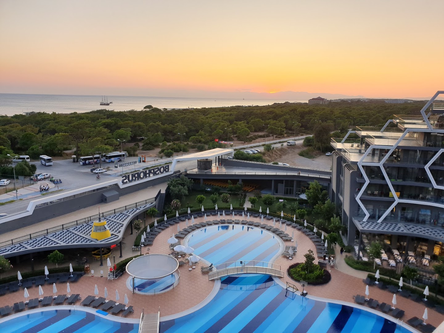 Bosphorus Sorgun Hotel skats no augšas uz baseinu kompleksu un jūru saulrietā, Sorgunā, Turcijā — moderna arhitektūra un priežu mežs