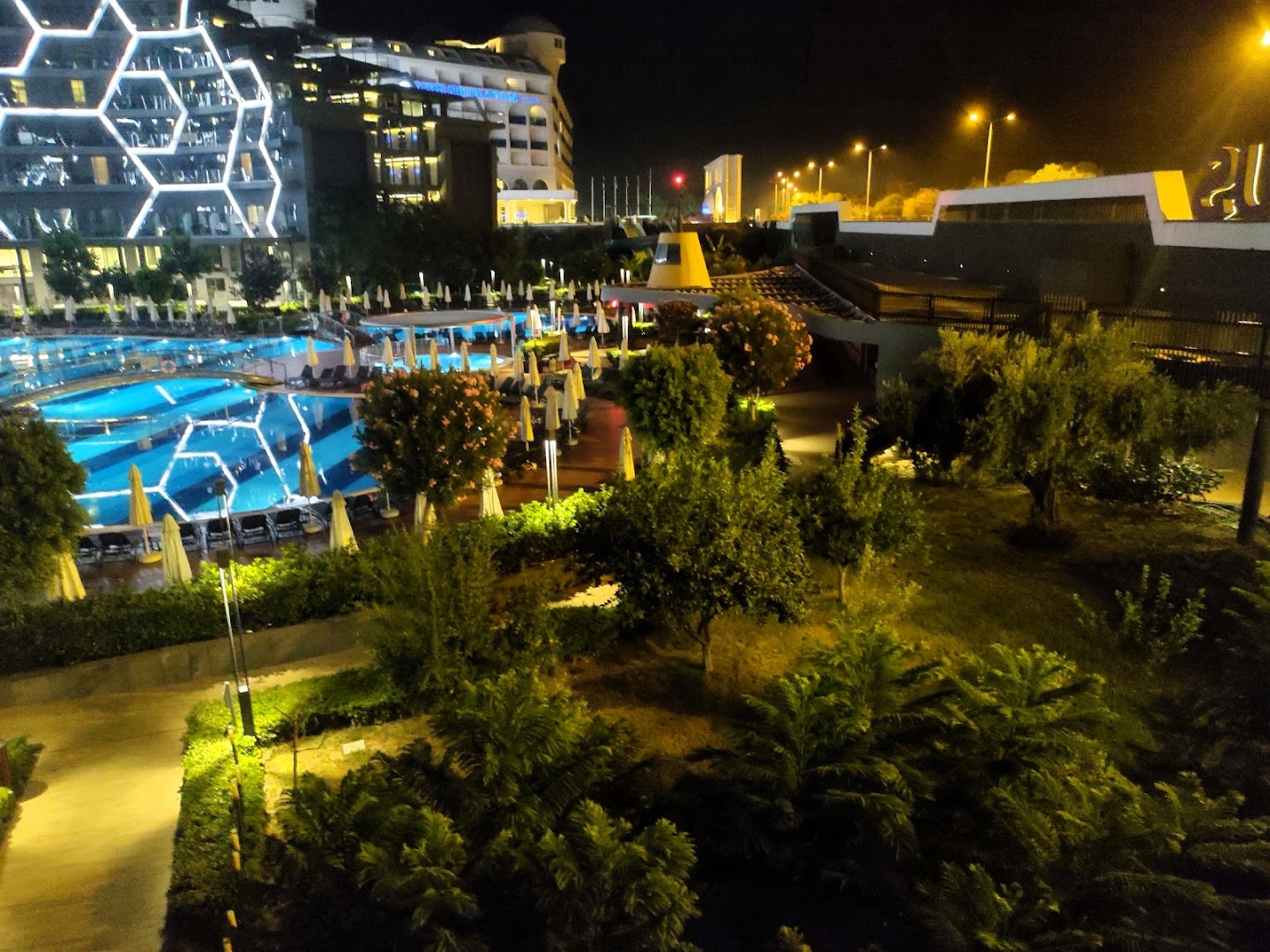 Bosphorus Sorgun Hotel izgaismotais baseins un dārzs nakts laikā — mājīgs apgaismojums, palmas un viesnīcas fasādes gaismas