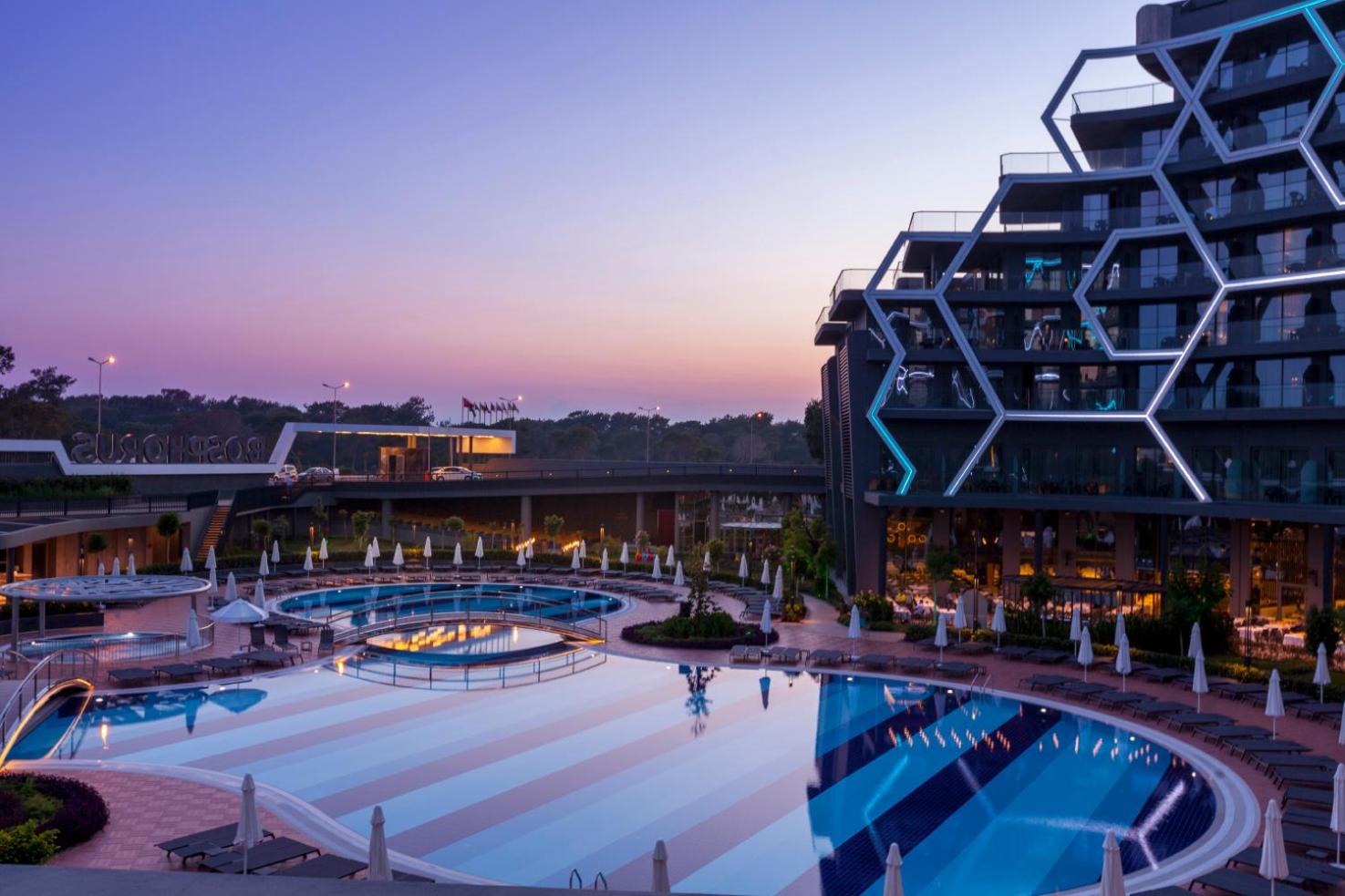 Bosphorus Sorgun Hotel baseina zona saulrieta laikā ar skatu uz viesnīcas korpusu un apkārtni — mierīga atmosfēra un vakara debesis