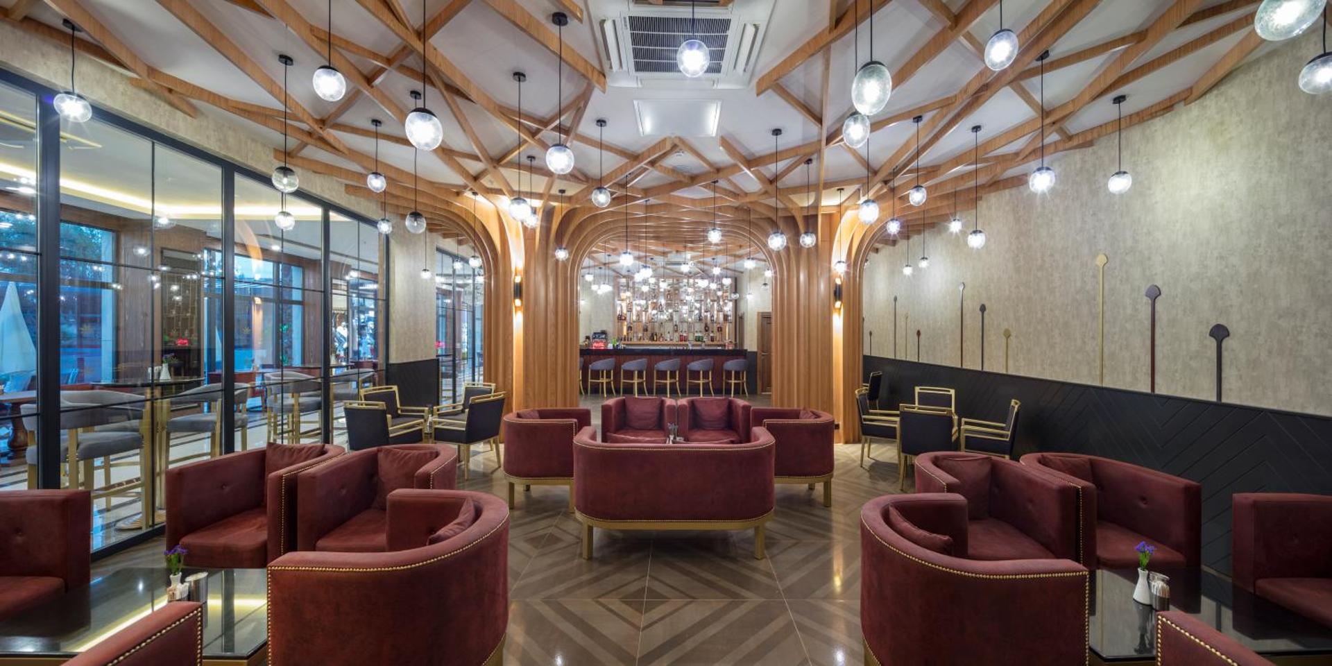Aydinbey Queen's Palace & SPA stilīgais atpūtas bārs ar tumši sarkanām mēbelēm, koka griestu dekorācijām un modernu apgaismojumu Turcijā.