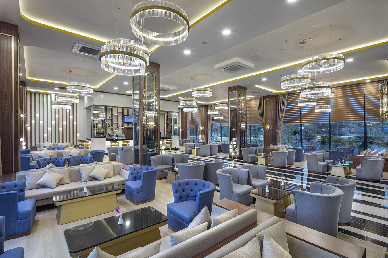 Aydinbey Queen's Palace & SPA plašā lobija atpūtas zona ar elegantiem dīvāniem, atpūtas krēsliem un greznām kristāla lustrām Belekā, Turcijā.
