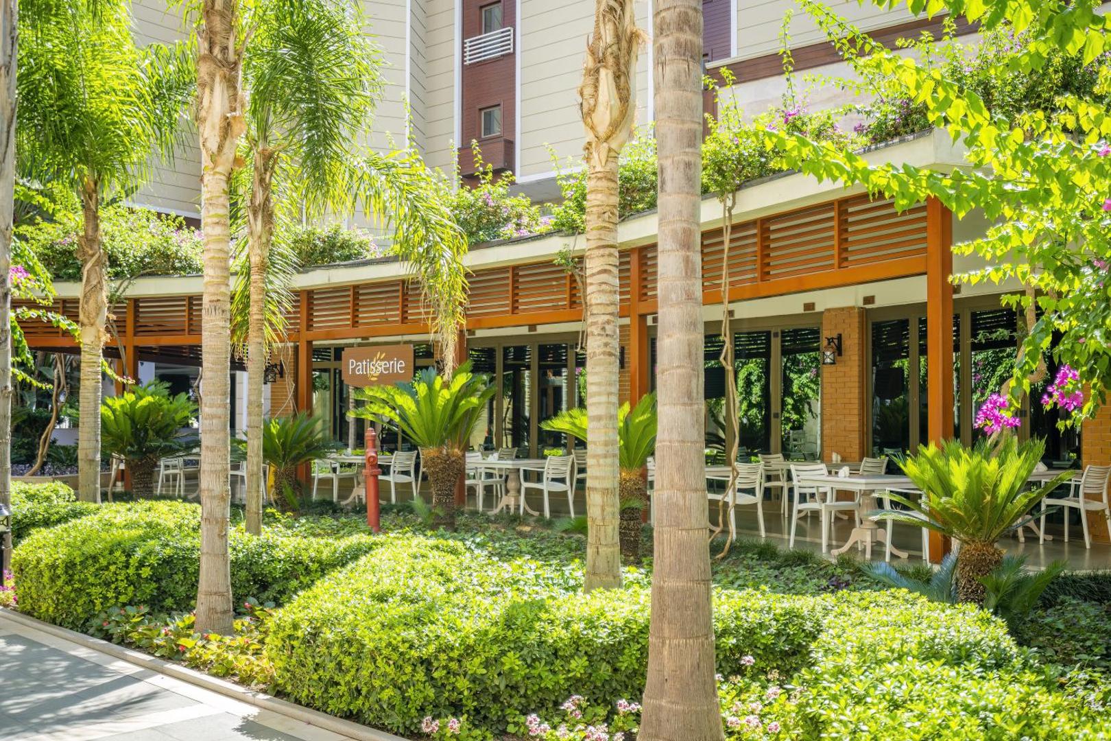 Mirada Del Mar Hotel konditoreja Patisserie ar āra terasi, ko ieskauj palmas un zaļumi Kemeras kūrortā.