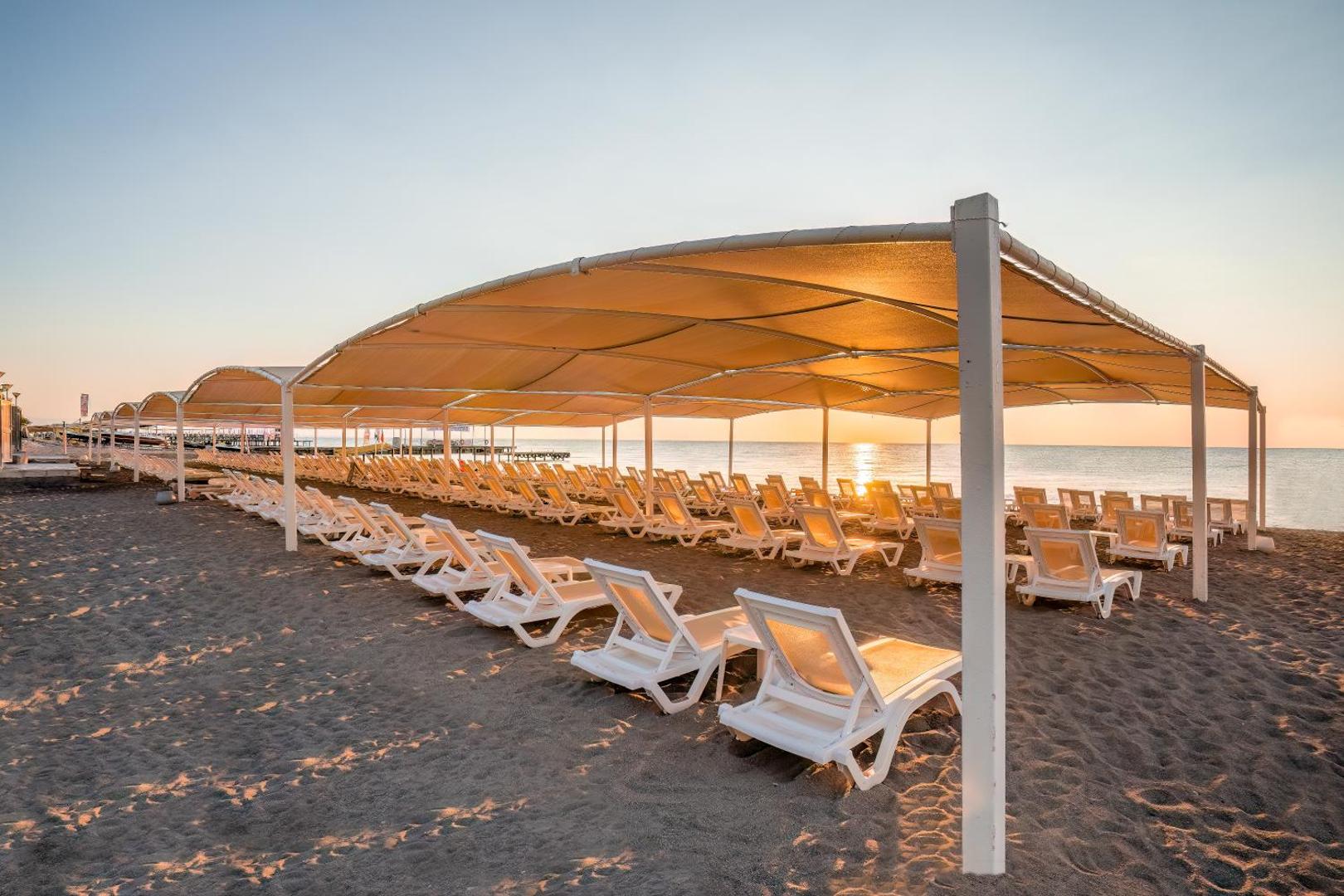 Mirada Del Mar Hotel smilšu pludmale ar sauļošanās krēsliem zem lielas nojumes saulrieta gaismā Kemeras reģionā, Turcijā