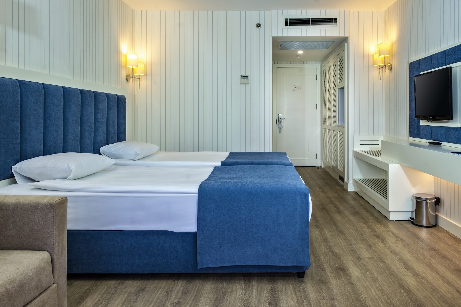 Mirada Del Mar Hotel numura interjers ar divvietīgu gultu, zilu galvgali un iebūvētu skapi gaišos toņos
