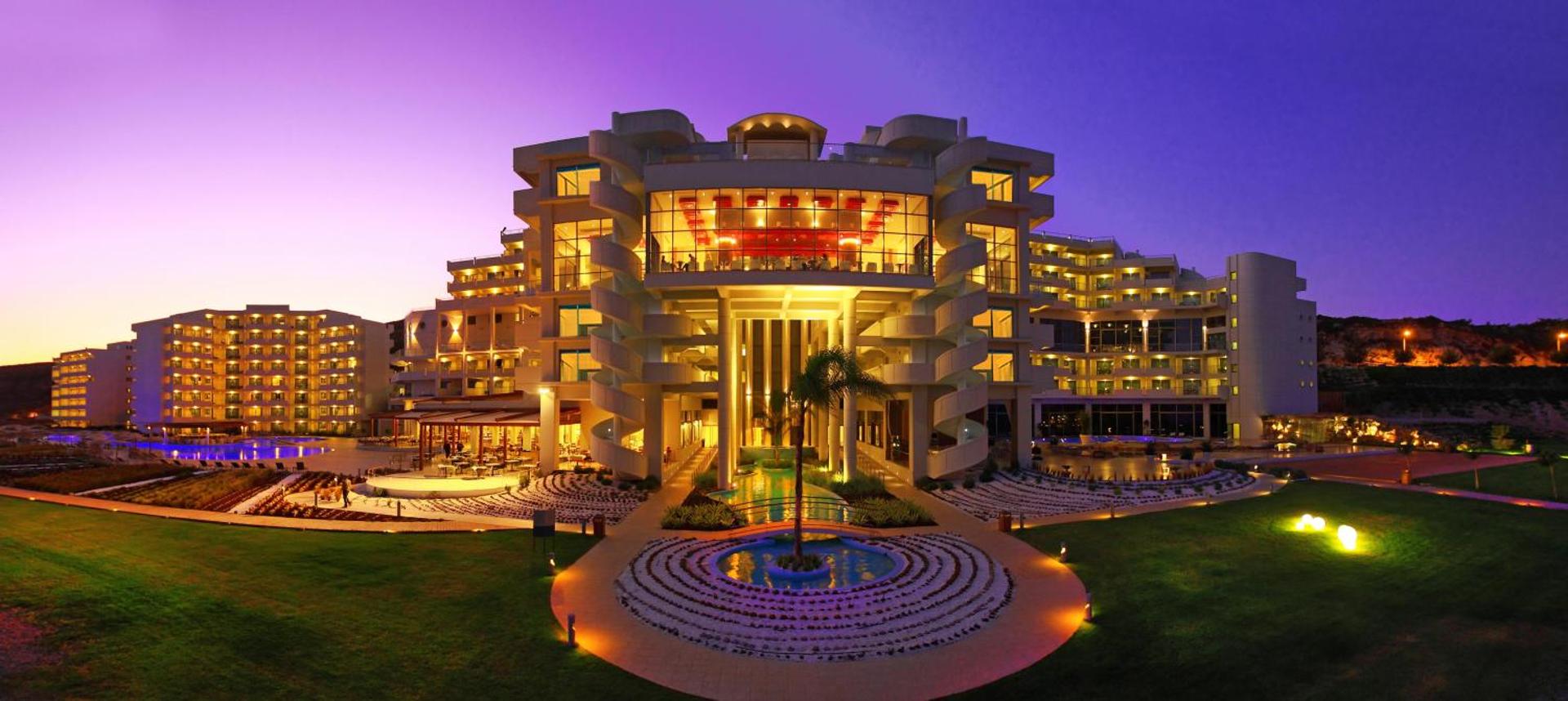 Elysium Resort & Spa galvenā ēka vakarā Faliraki piekrastē Rodas salā — izgaismota arhitektūra ar modernām kāpnēm un dārza ainavu