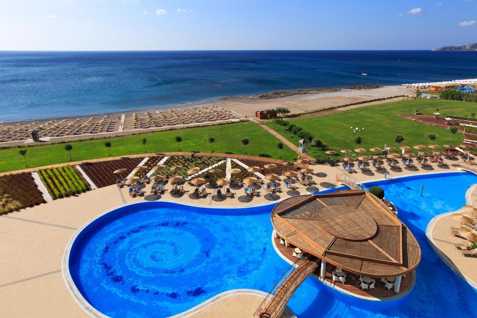 Elysium Resort & Spa panorāmas skats uz baseinu, zālāju un privāto pludmali ar saulessargiem Rodas piekrastē