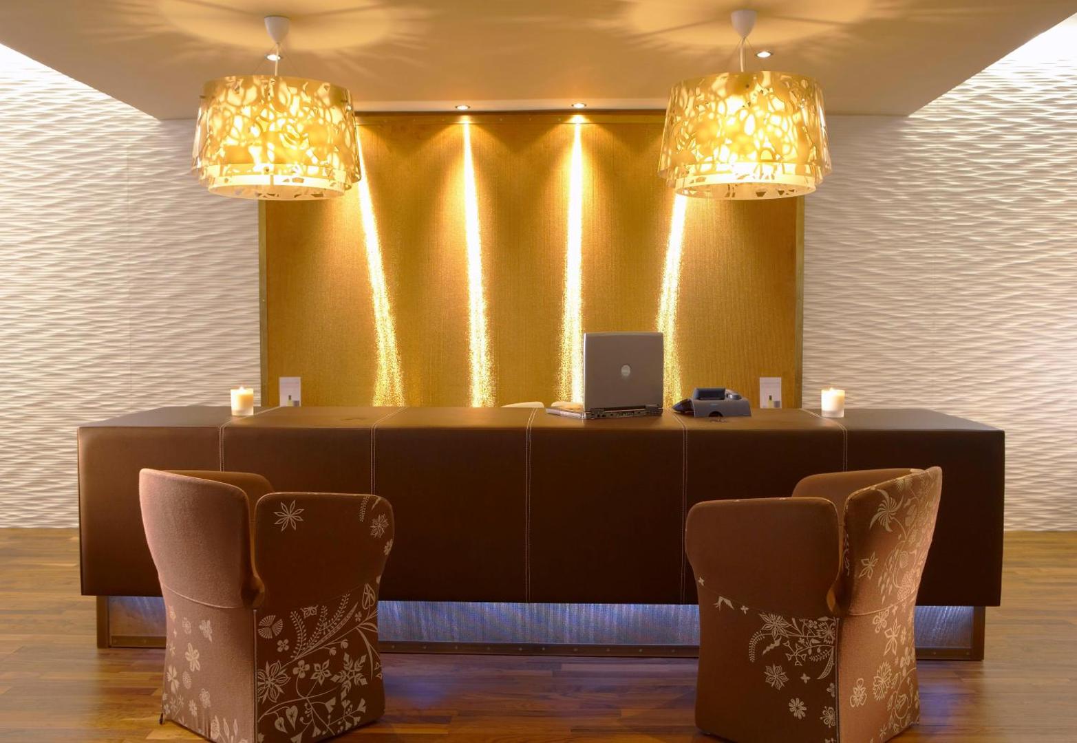 Elysium Resort & Spa viesnīcas recepcijas zona Rodas salā ar modernu dizainu, zeltītu sienas dekoru un ērtiem atpūtas krēsliem