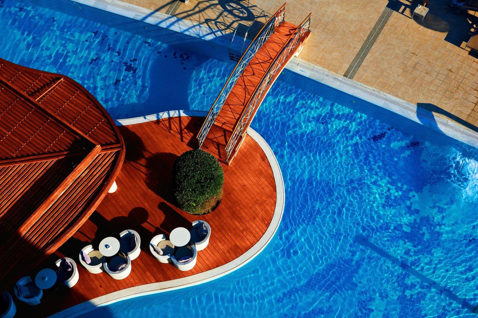 Elysium Resort & Spa baseina bāra koka terase un dekoratīvs tiltiņš pār zilo ūdeni Rodas kūrortā
