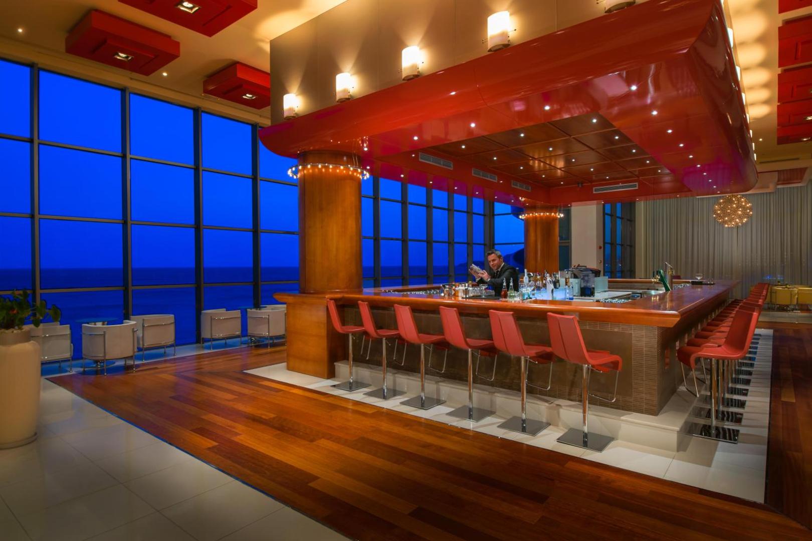 Elysium Resort & Spa moderns bārs ar sarkanu interjeru un panorāmas logiem uz jūru vakara stundā Rodas salā