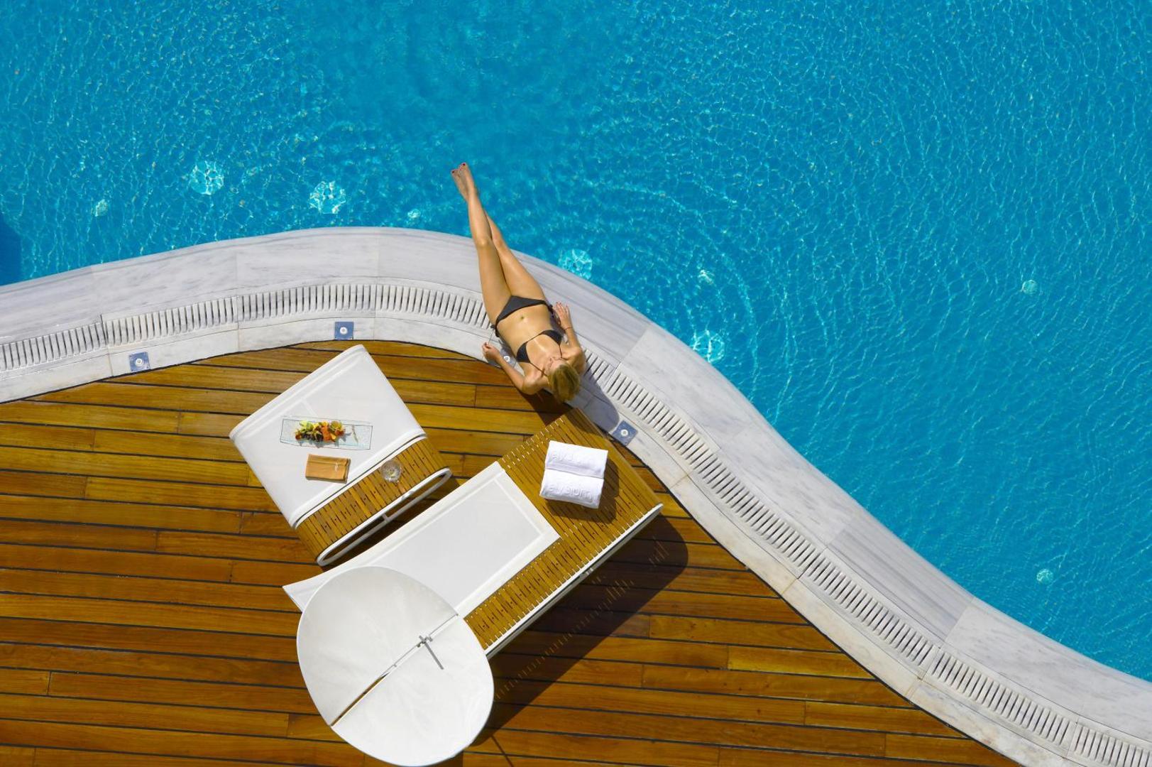 Elysium Resort & Spa atpūtas zona pie baseina ar modernu sauļošanās krēslu un koka klāju Rodas salā