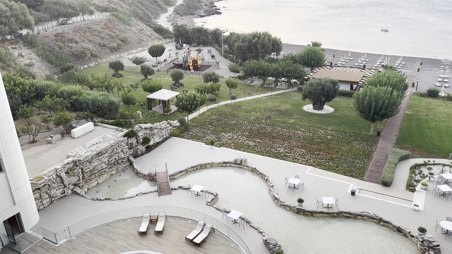 Elysium Resort & Spa teritorijas skats no augšas — dārzs, bērnu rotaļu laukums, atpūtas terases un pieeja oļu pludmalei