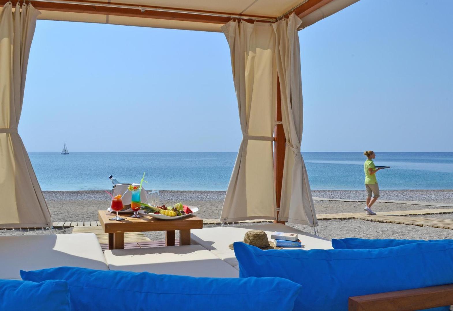 Elysium Resort & Spa pludmales nojume ar kokteiļiem un augļu plati, fonā redzama jūra un apkalpojošais personāls