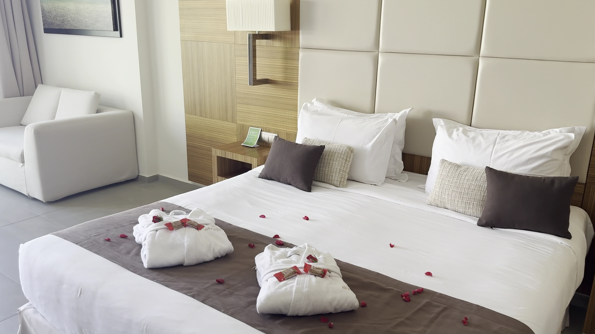 Elysium Resort & Spa viesnīcas numura gulta ar halātiem un rožlapiņām — romantiska sagaidīšana Rodas salā