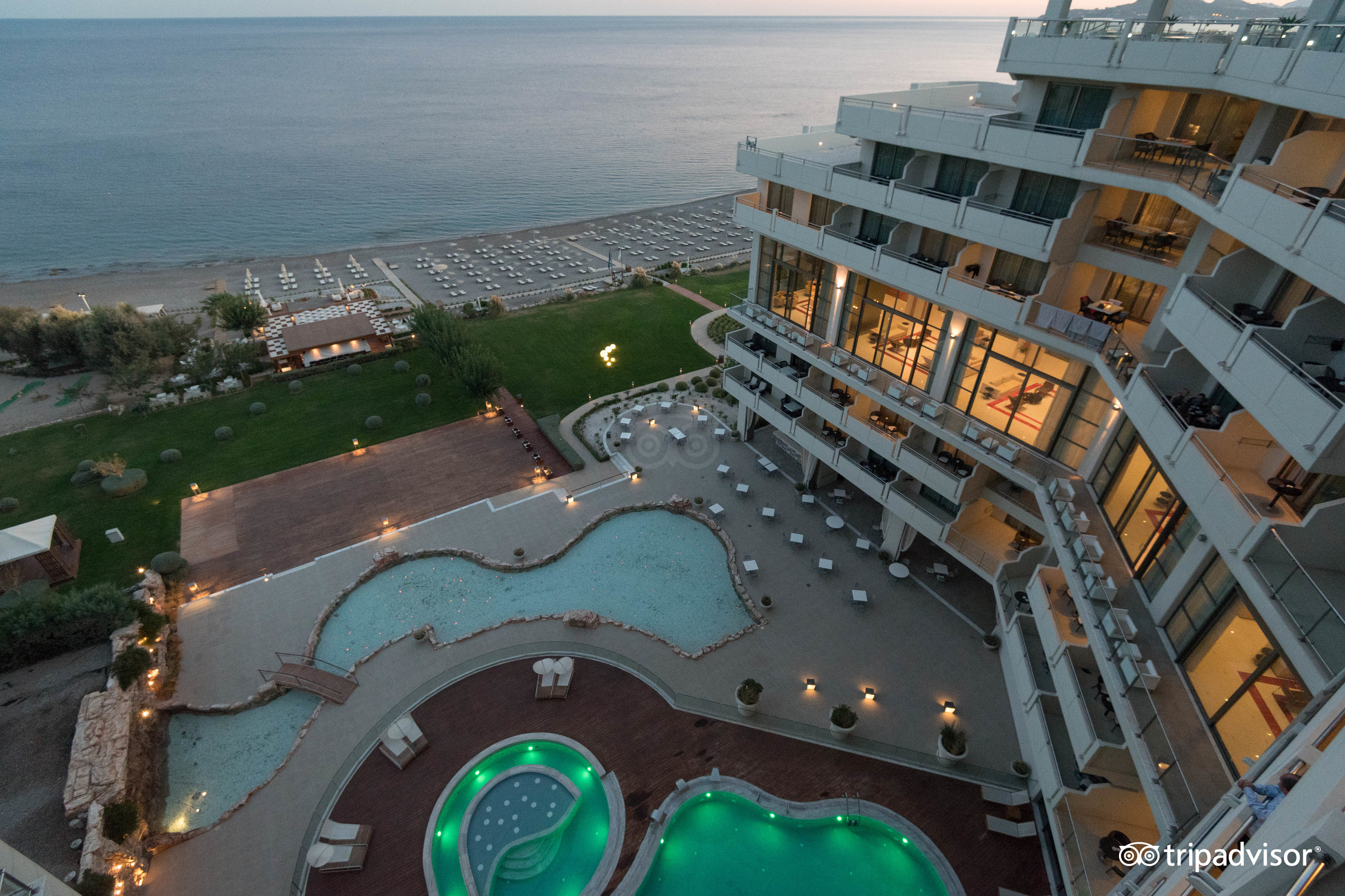 Skats no augšas uz Elysium Resort & Spa baseiniem un privāto pludmali — terases ar galdiņiem un skats uz Egejas jūru