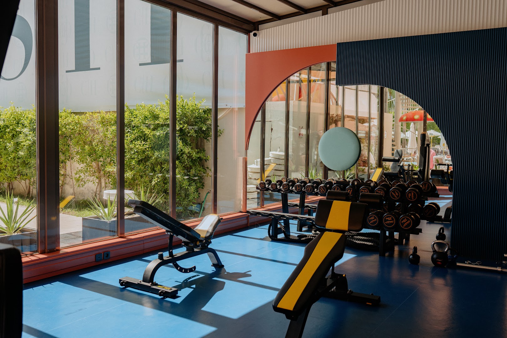 Castival Hotel modernā fitness zāle ar svariem, soliem un panorāmas logiem uz dārzu un āra zonu