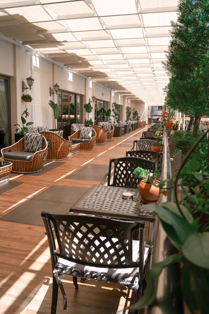 Castival Hotel āra terase ar pītiem krēsliem un galdiņiem zem nojumes, ko ieskauj zaļumi un dekoratīvie augi podos
