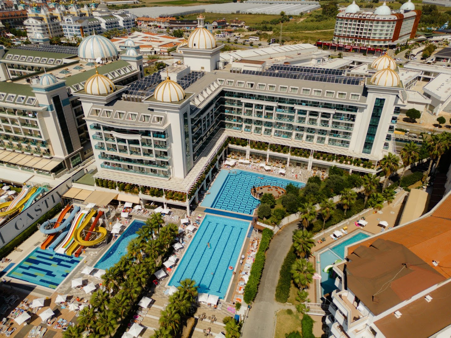 Castival Hotel aerofoto ar plašo baseinu kompleksu un viesnīcas ēku Sidē — redzami vairāki peldbaseini, sauļošanās krēsli un apkārtējā infrastruktūra