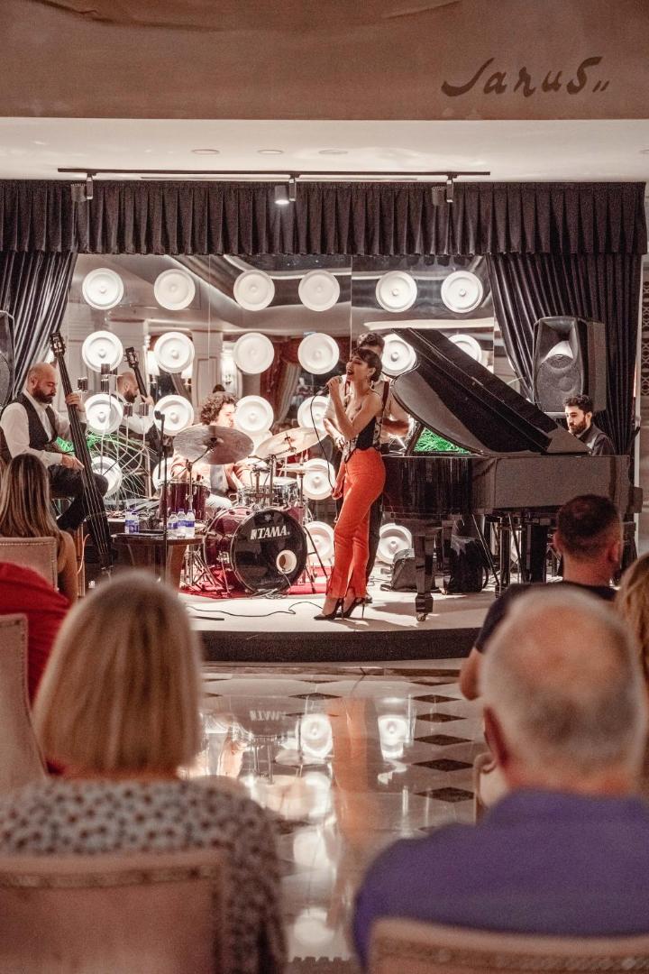 Castival Hotel dzīvās mūzikas vakars ar džeza grupu, dziedātāju un klavierēm uz skatuves viesnīcas zālē