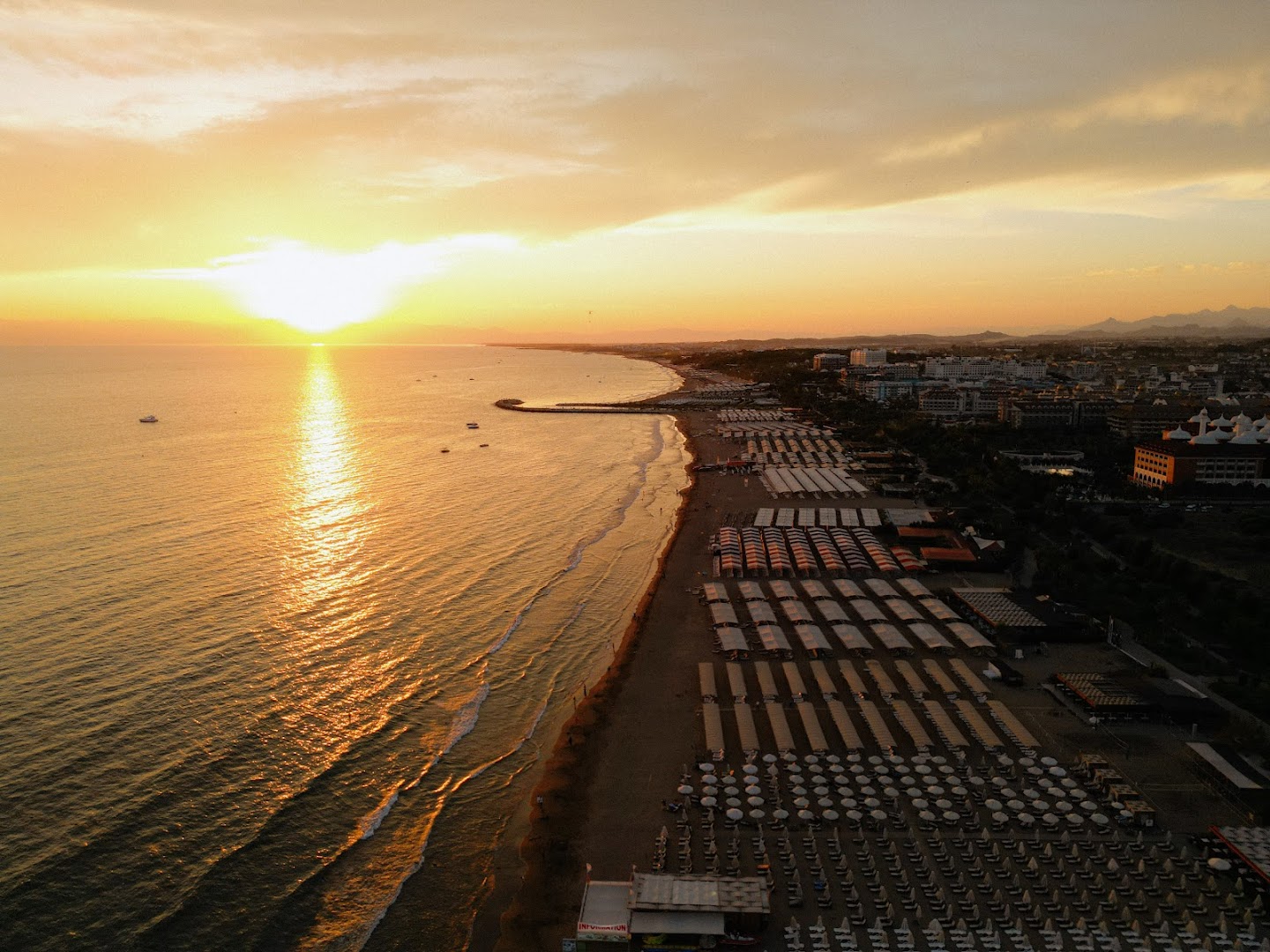 Castival Hotel skats no putna lidojuma uz plašo smilšu pludmali saulrieta laikā Sidē, Turcijā — jūra, saulessargi un pilsētas panorāma