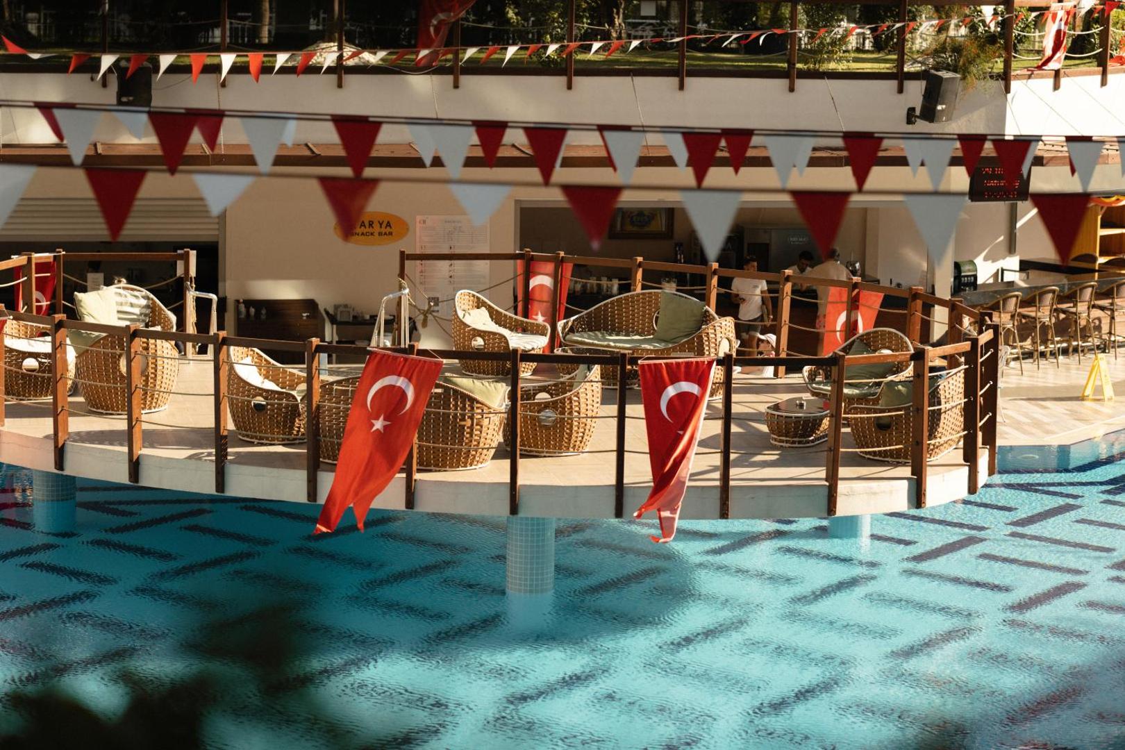 Castival Hotel uzkodas bārs virs baseina ar pītiem krēsliem un Turcijas karogiem — atpūtas terase ūdens malā